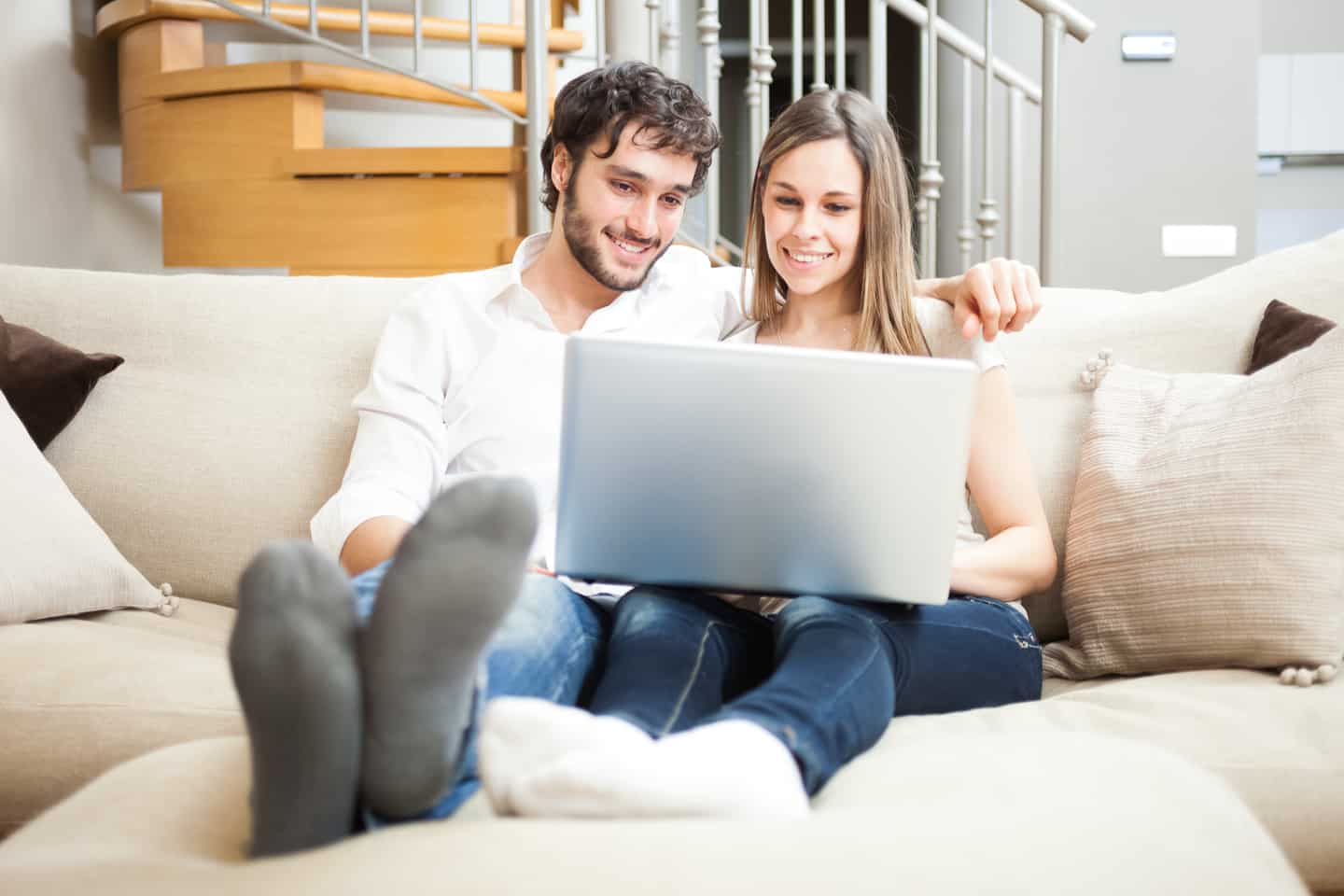 young man and woman sitting on couch looking at laptop