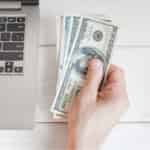 person holding cash next to laptop