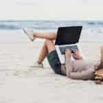 person laying on the beach working on laptop