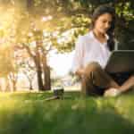 woman sitting on grass working on a laptop